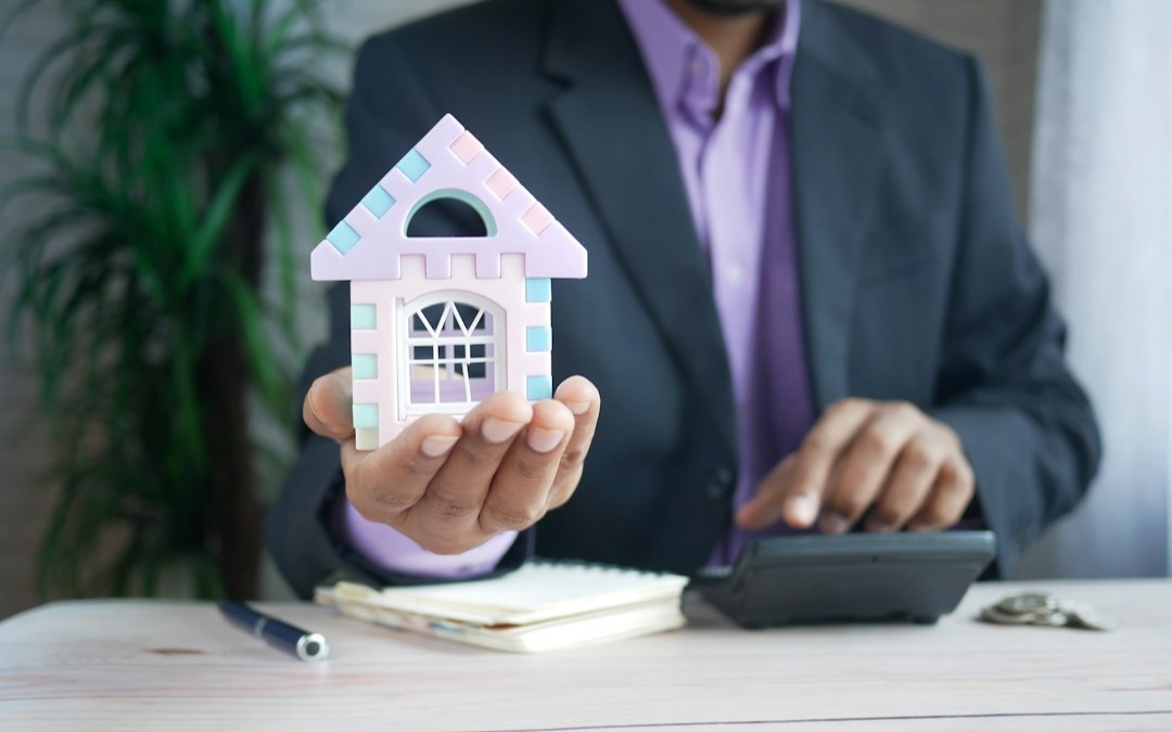 man holding model house at desk with calculator